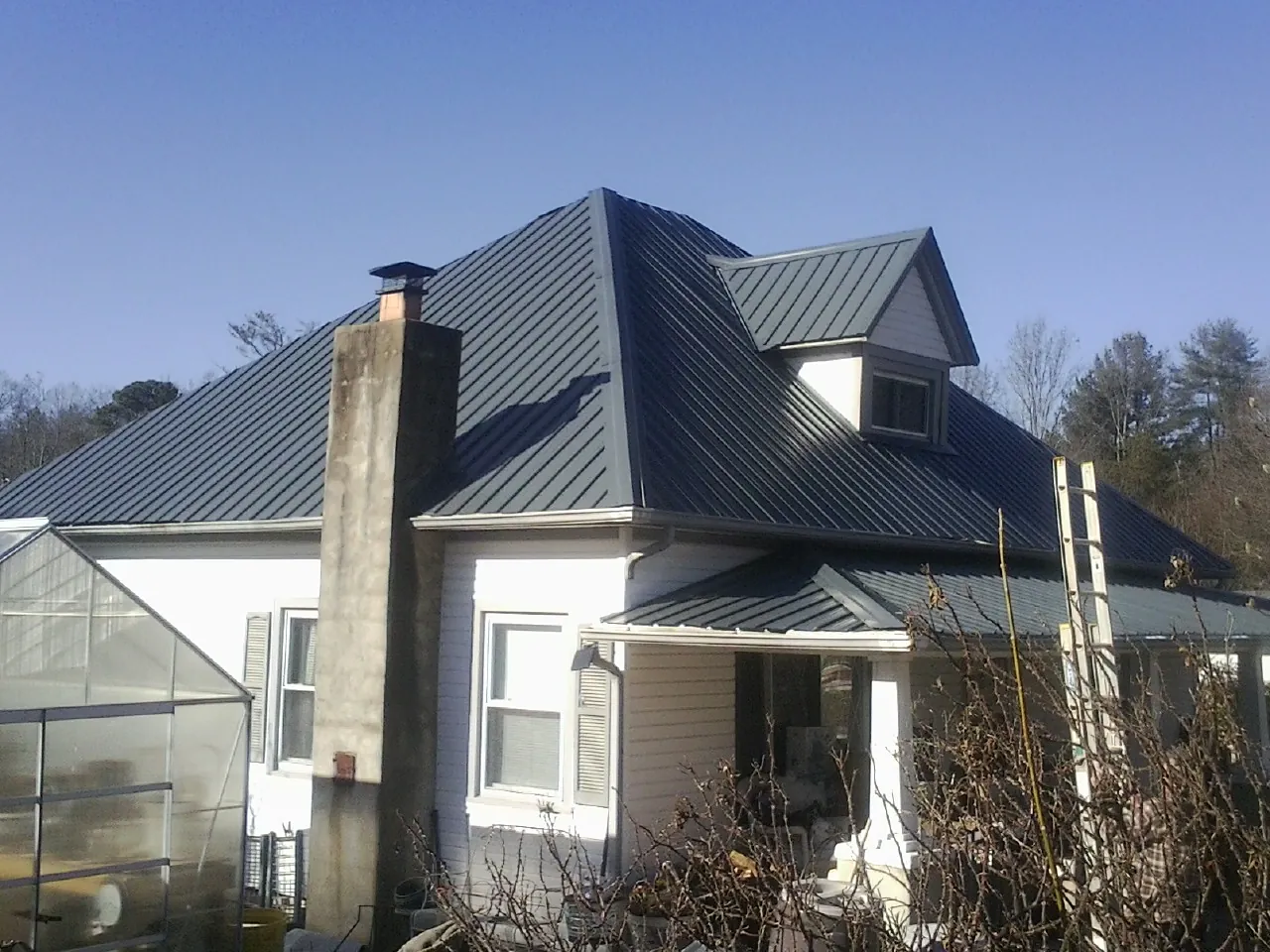Dark blue standing seam metal roof on a white farmhouse with dormer — Slate & Tile Roof Repair by Roofing Brothers in Smithville Flats