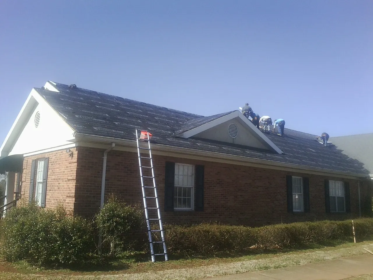 Crew tearing shingles off a brick ranch roof with a ladder set — Metal Roof Repair work by our crew in Smithville Flats