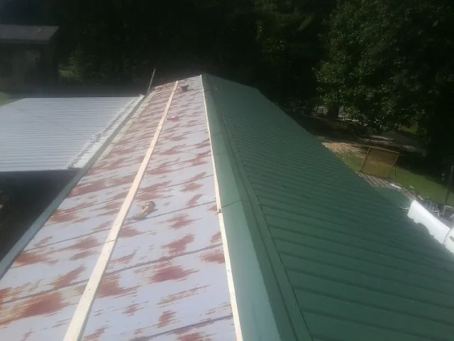 Old rusted panels beside newly installed green metal roofing — Wind Damage Roof Repair by Roofing Brothers in Smithville Flats