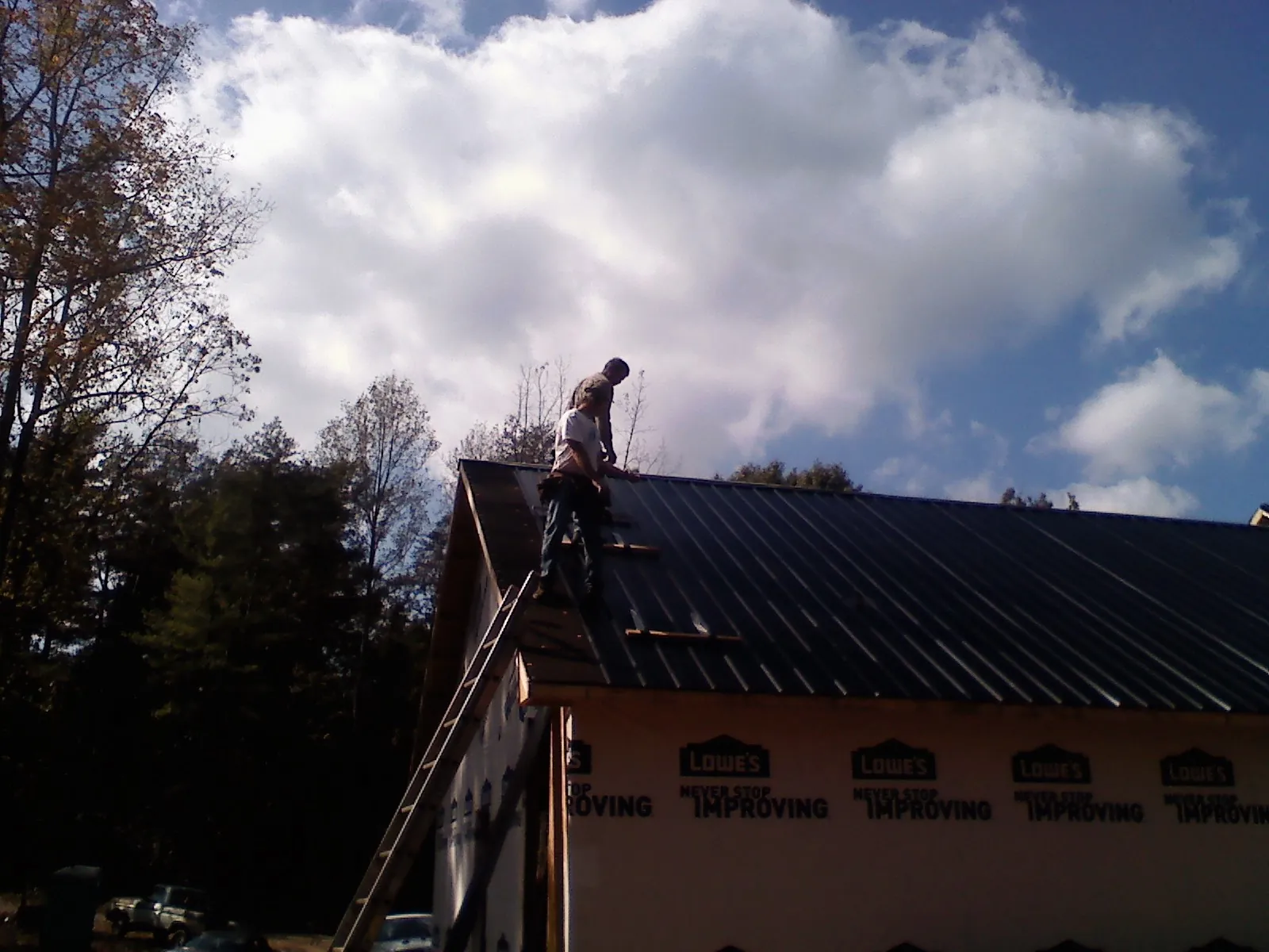 Roofer fastening dark metal panels high against a cloudy sky, from a Roof Inspection job in Smithville Flats