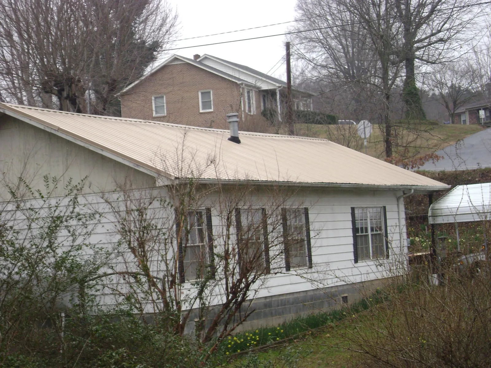 Tan metal roof on a white sided house set into a hillside — Commercial Roofing by Roofing Brothers in Smithville Flats