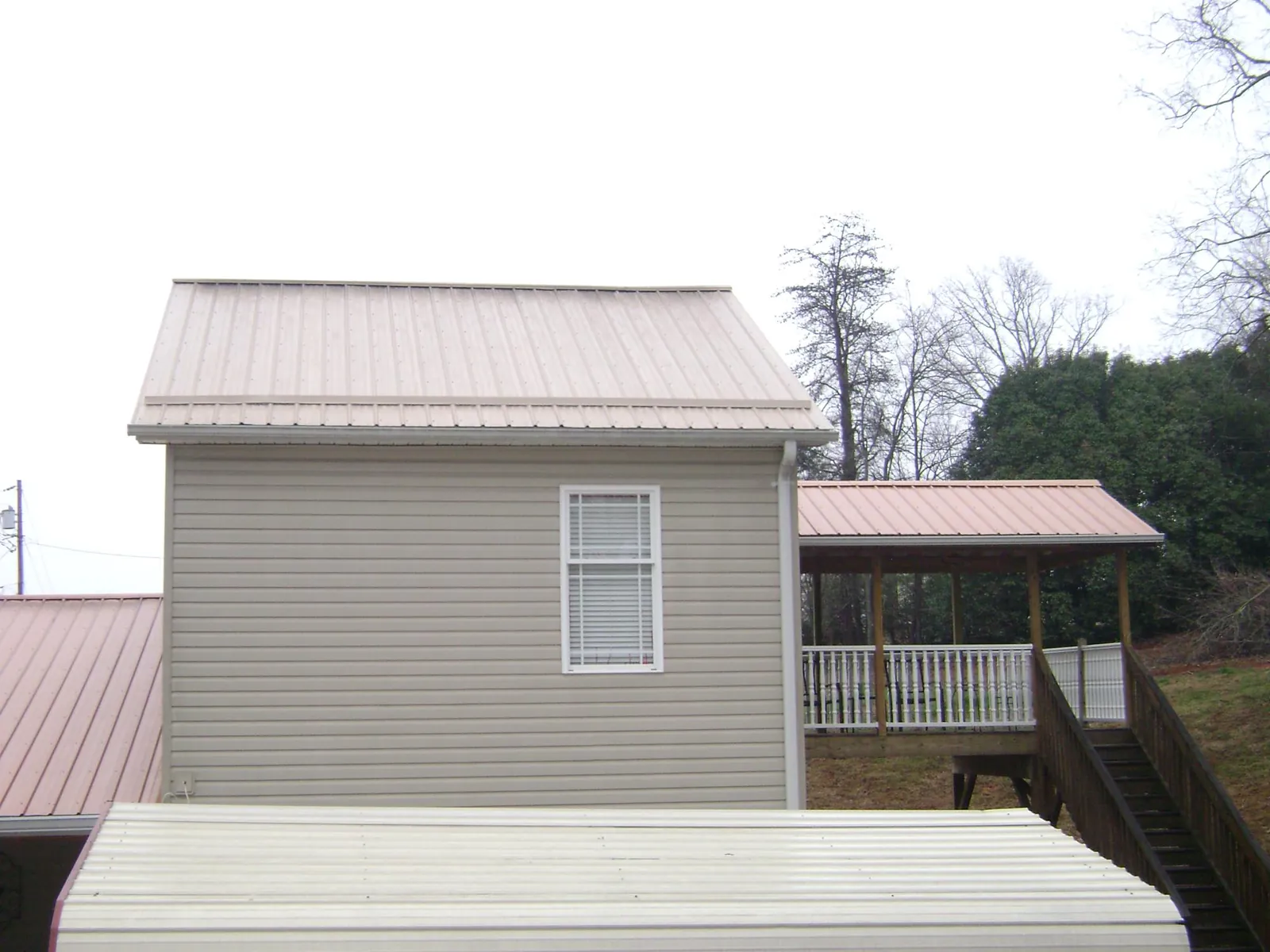 Tan metal roofs on a two story addition and attached porch, from a Roof Replacement job in Smithville Flats